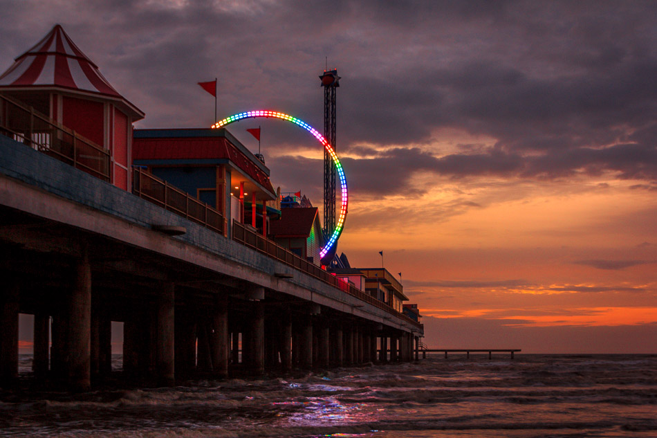 The rainbow-colored lights of a thrill ride on Galveston, Texas’ Pleasure Pier pierce the dawn’s twilight.